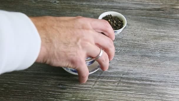 Человеческая рука забирает один маленький сосуд с чайными листьями и кладет большой — стоковое видео