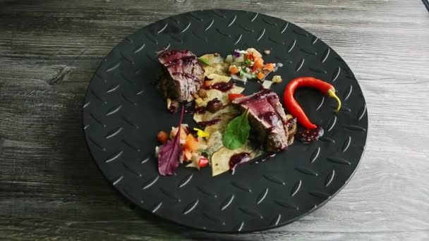 Hand rotates black plate with roasted meat pieces, potato chips, and vegetable salad — ストック動画