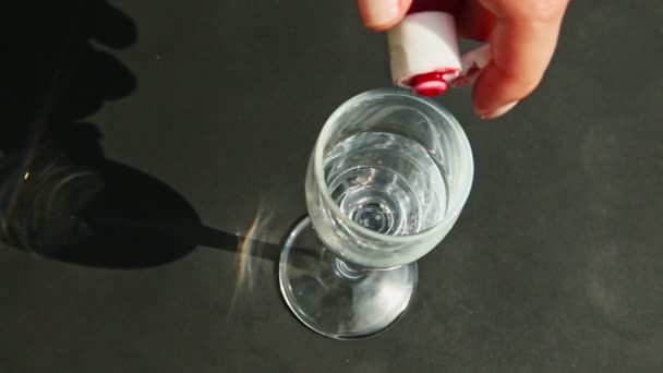 Top view woman hand drips red colorant on water in tall wine glass — Stock Video