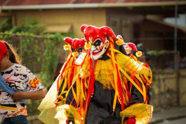 Concepcion De La Vega, DOMINICAN REPUBLIC - FEBRUARY 11, 2019: group of men in clown masks walks under rain by city street at dominican carnival on February 11 in Concepcion De La Vega
