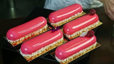 Hindistancevizi talaşı ve ahududu ile süslenmiş beş pembe renkli oval pastadan birinde menekşe çiçeğiyle dekore etme süreci