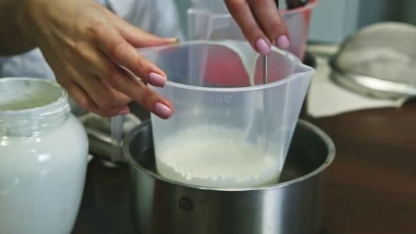 閉じられた女性の手はゆっくりと木製のキッチンテーブルの上に立つプラスチック製のペアで白いホイップクリームを攪拌 — ストック動画