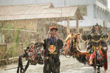 Concepcion De La Vega, DOMINICAN REPUBLIC - FEBRUARY 11, 2019: adult man carries two big masks under strong rain by city street at dominican carnival on February 11 in Concepcion De La Vega