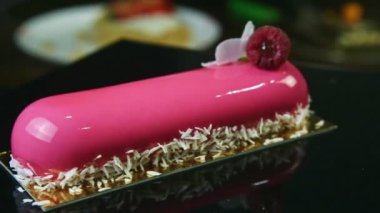 Kapalı pembe kaplama oval ekinler hindistan cevizi talaşı, beyaz çiçek ve ahududu ile süslenmiş siyah standın etrafında dönüyor.