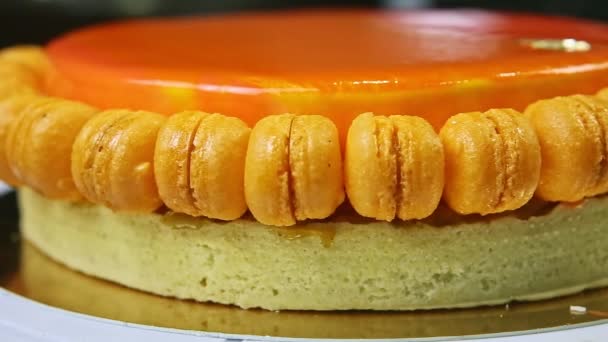 Nahaufnahme-Panorama bei ganzer orange glasierter Biskuittorte mit Makronen — Stockvideo