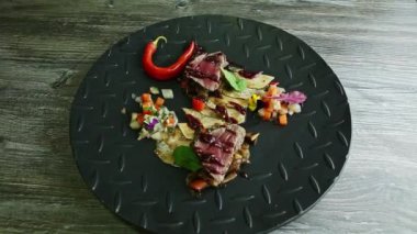 Kızarmış et parçalarını patates cipsi ve siyah tabakta sebze salatasıyla yakınlaştır.