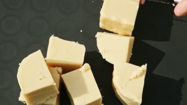 Kadın eli bıçakla kesilir. Büyük beyaz ev yapımı badem ezmesi kübü.