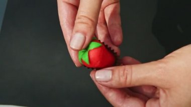 Üst kattaki kadın elleri kırmızı çilek şekilli badem ezmesi şekeri gösteriyor.
