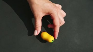 Kadının üst görüntüsü armut şeklindeki badem ezmesi şekerini kırmızı renkli püsküllerle boyuyor.