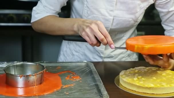 Banketbakker zet ronde oranje geglazuurde kaastaart op amandel tussenlaag — Stockvideo