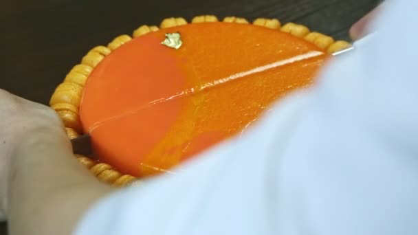 Closeup hands cut on half by big knife round cheesecake with orange mirror glaze — Stock Video