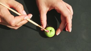 Ellerin üst görüntüsü elma şekilli badem ezmesi şekerini kırmızı renkli püsküllerle boyar