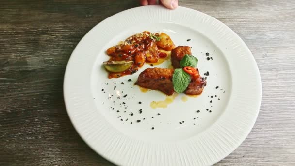 Human hand rotates plate with roasted meat ribs, sauce, and garnish — Stock Video