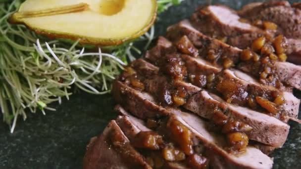 Top macro zicht op fijn versierde schotel van geroosterd vlees plakjes draait op zwarte plaat — Stockvideo