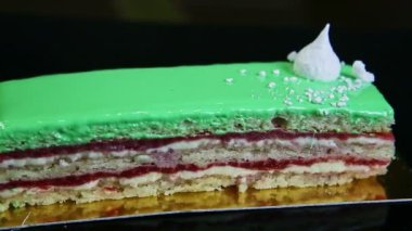 Kapalı siyah tepsi ile bir porsiyon yeşil katmanlı pasta etrafında döner