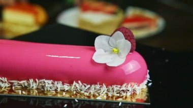 Kapalı pembe kaplamalı oval pasta, çiçekli ve ahududulu siyah standda dönüyor.