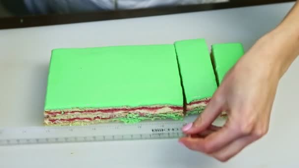 Il pasticcere ritaglia su porzioni da coltello la torta smaltata verde con riempitura fruttata alla panna — Video Stock