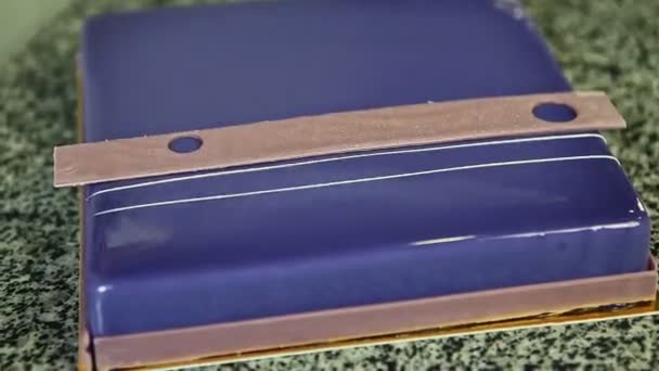 Detailní celý fialový prosklené čtvercové pěny dort s čokoládovou výzdobou — Stock video