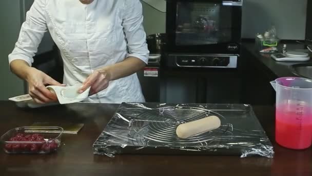 Кондитер вынимает замороженную форму овального торта и кладет на металлический стенд — стоковое видео