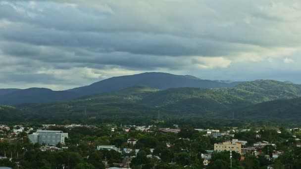 Медленно панорама на маленький городок с зеленью среди гор и пушистыми облаками — стоковое видео