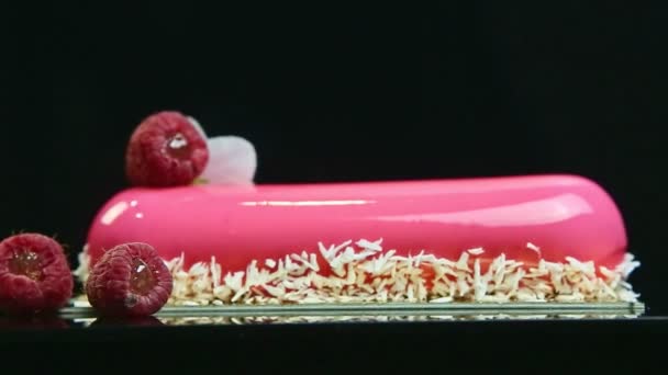 Closeup focus out from pink glazed oval cake with coconut shavings and raspberries — Stock Video