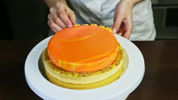 Confectioner decorate orange glazed round cheesecake by small yellow macaroons — Stockvideo