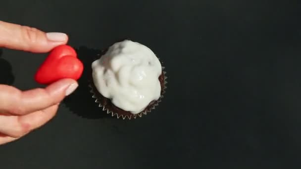 Mani vista dall'alto mettere caramelle cuore marzapane rosso su bianco glassato cioccolato cupcake — Video Stock