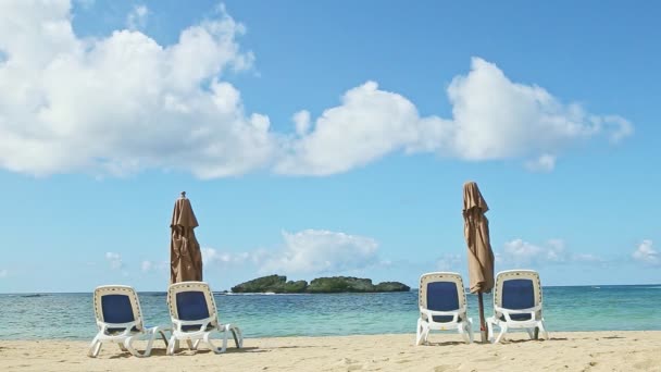 Большие пушистые облака летают над океаном и песок с пляжными стульями и закрытыми зонтиками — стоковое видео