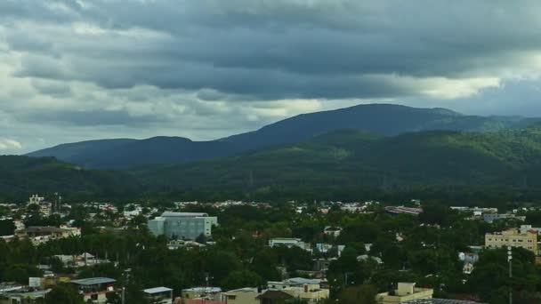 Крупним планом панорама маленького міста на тлі пухнастих білих хмар над блакитними горами — стокове відео