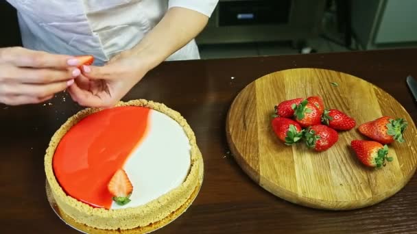 Konditor legt Hälfte der reifen roten Erdbeere auf runden, bunt glasierten Käsekuchen — Stockvideo