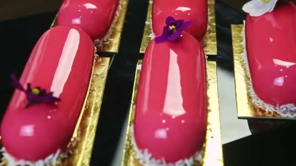 Вид зверху крупним планом багато рожевих глазурованих десертів з квітковим прикрасою на чорному лотку — стокове відео