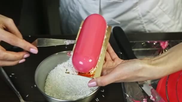Nahaufnahme Konditor dekorieren rosa glasierte Mousse-Kuchen mit Kokosraspeln — Stockvideo