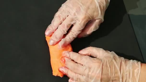 Vue de dessus sur les mains de la femme dans les gants pétrir grand morceau de masse de massepain orange vif — Video