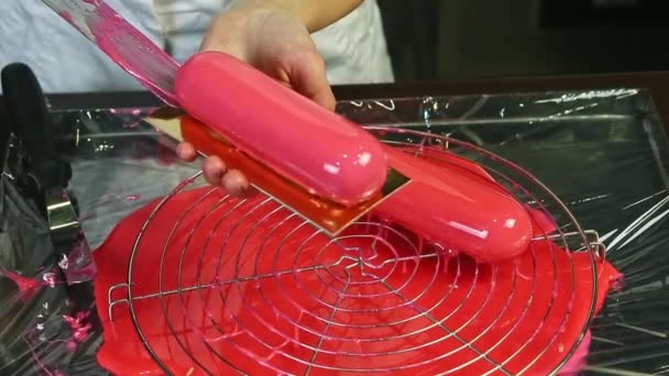 Top view closeup confectioner puts by knife pink glazed oval dessert on golden stand — Stock Video