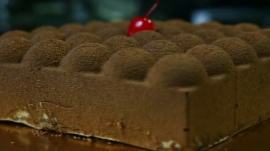 Kırmızı kirazla dekore edilmiş kare çikolatalı pasta etrafında döner.