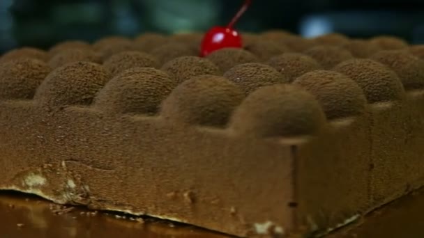 Closeup bolo de chocolate quadrado inteiro decorado com cereja vermelha gira em torno — Vídeo de Stock