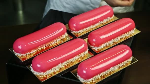 Confectioner by hands decorating by raspberry one of five pink glazed oval desserts — Stock Video