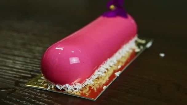 Confeiteiro corta por faca na metade rosa vitrificada bolo oval cremoso com flor violeta — Vídeo de Stock