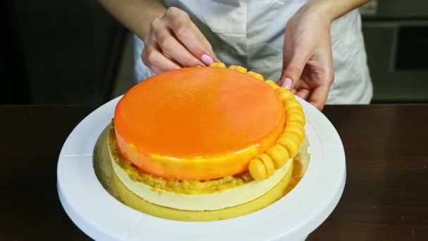 Kvinna i kock uniform dekorera orange glaserad cheesecake av mini makaroner — Stockvideo