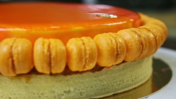 Primo piano panorama a sinistra a tutto tondo torta di formaggio arancio glassato con mini macaron — Video Stock