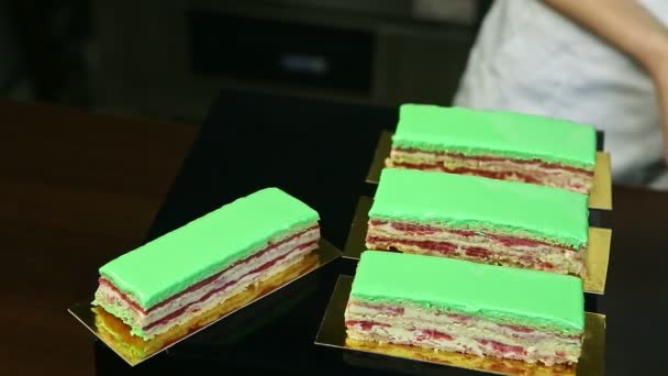 Banketbakker in wit uniform zet porties groene geglazuurde crème fruitige gelaagde taart — Stockvideo