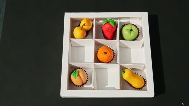 Vista superior en la mano de la mujer pone frutas en forma de caramelos de mazapán en la caja de regalo blanca — Vídeos de Stock