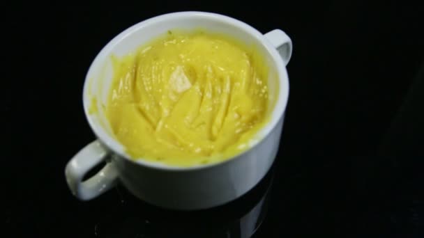 Top view focus in on yellow custard cream in white cup on black background — Stock Video