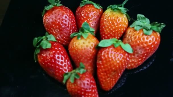 Vue de dessus mise au point sur un petit groupe de fraises rouges mûres entières sur surface noire — Video