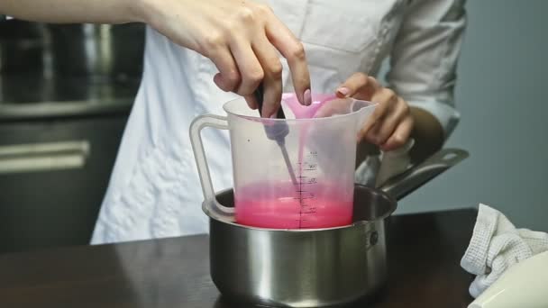 Confectioner in chef uniform slowly stirs homemade pink liquid glaze in plastic pail — Stock Video