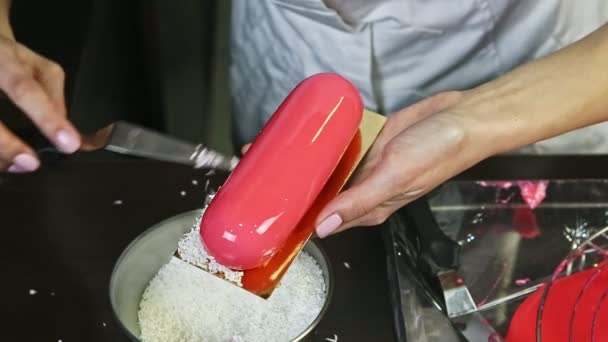 Closeup process of decorating pink glazed oval cream dessert by coconut shavings — Stock Video