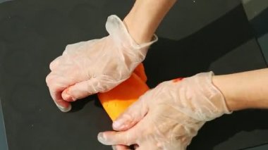 Eldivenli kadın ellerinin üst görüntüsü büyük bir parça turuncu badem ezmesi yoğurur.