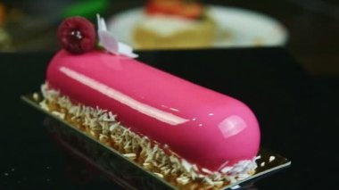 Kapalı pembe kaplamalı oval tatlı, çiçekli ve ahududulu, siyah stantta dönüyor.