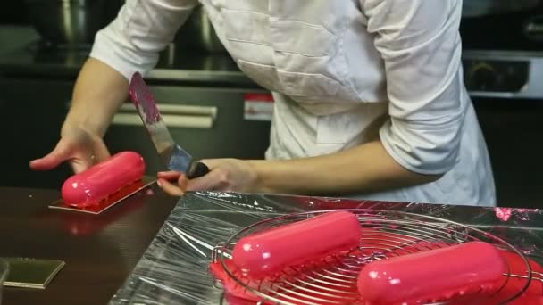 Banketbakker in chef-kok uniform zet roze geglazuurd ovaal dessert op gouden standaard — Stockvideo