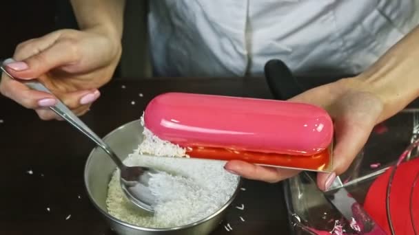 Nahaufnahme Prozess der Dekoration rosa glasiert ovales Dessert durch Kokosraspeln — Stockvideo